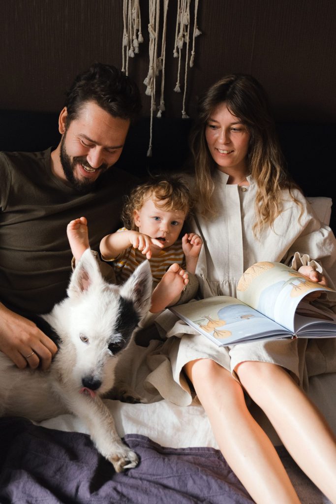 Famille avec un enfant et un animal de compagnie, partageant un moment de lecture sur un lit.